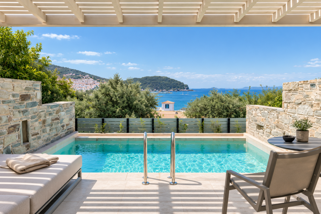 Outdoor pool terrace at Minnŏ Boutique Hotel & Spa on Skopelos, with stone walls, pergola shade, loungers and views across the Aegean Sea and hillside town.