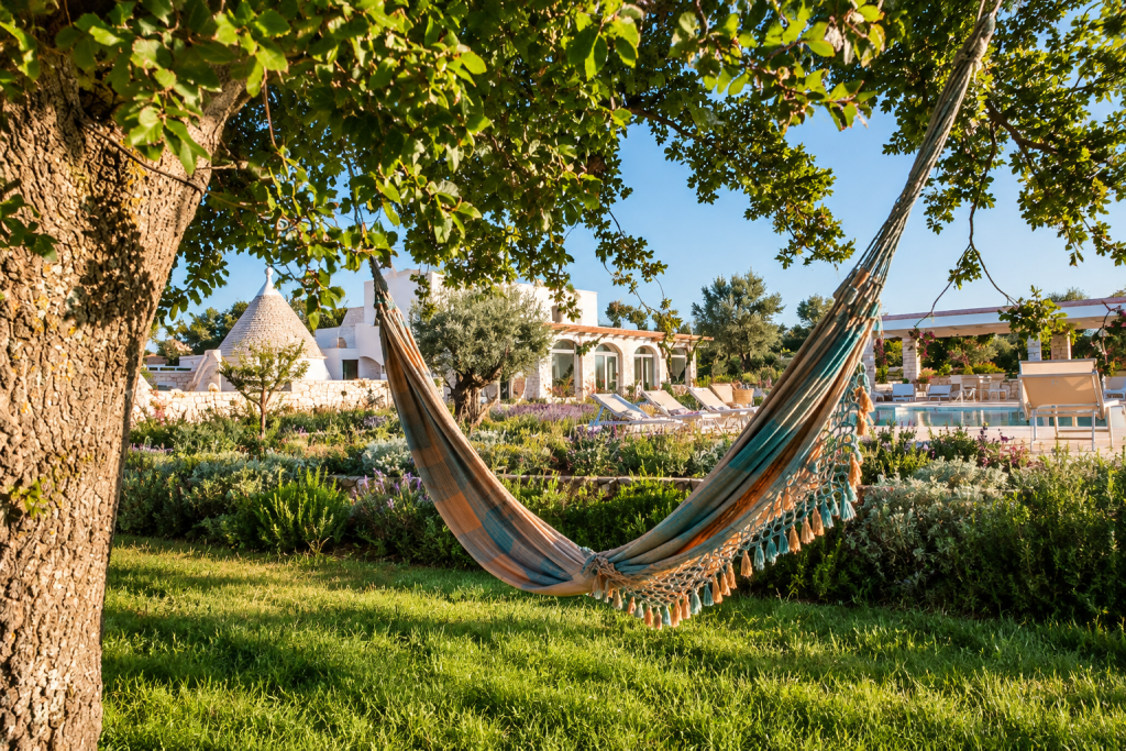 Hammock beneath a large tree in the gardens of Leonardo Trulli Resort near Locorotondo, overlooking the trulli, Mediterranean landscaping and swimming pool in warm afternoon light.
