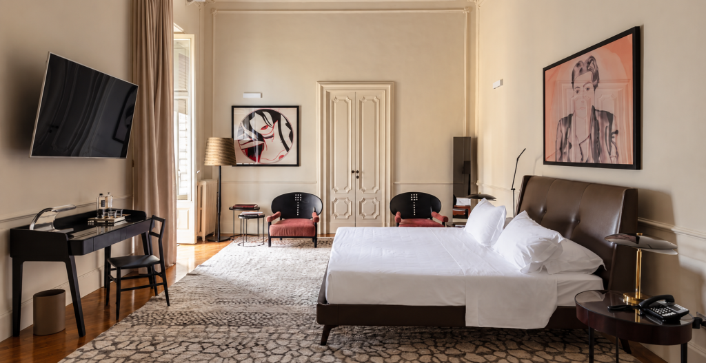 Suite bedroom at La Fiermontina Palazzo Bozzi Corso in Lecce, with a contemporary leather bed, classic paneled walls and doors, artwork, lounge chairs and warm natural light.