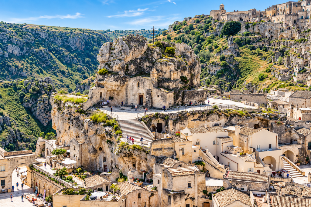 Panoramic view of Matera’s Sassi, with limestone cave dwellings, a rock-hewn church, stone stairways and terraces overlooking the surrounding ravine.