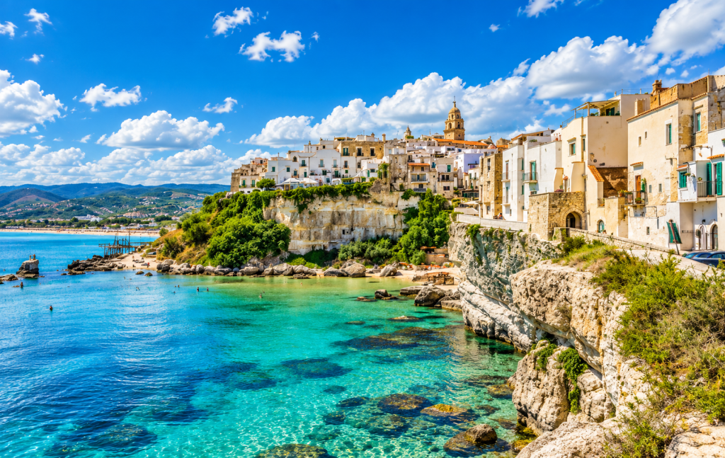 Coastal town of Otranto, Puglia, with pale limestone buildings perched above clear turquoise Adriatic water, rugged cliffs and a historic church tower.