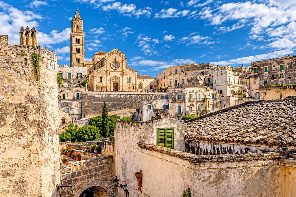 Historic hilltown in Puglia with weathered pale-stone buildings, tiled rooftops and a prominent church with a tall bell tower overlooking the densely built old town.
